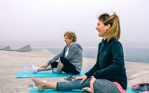 Young woman sitting on shore at beach against sky