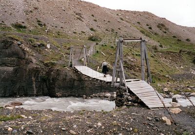 Woman walking on suspension footbridge over river