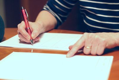 Midsection of woman writing on paper at table