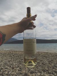 Close-up of hand holding bottle at beach against sky