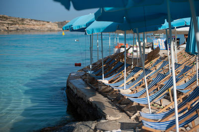 Deck chairs on rocks by sea against blue sky