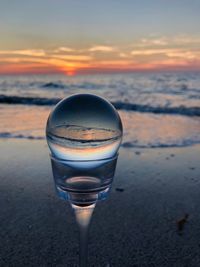 Close-up of beer on beach against sky during sunset
