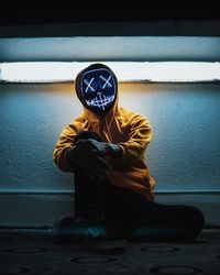 Man wearing illuminated mask sitting against wall