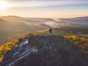 Rear view of man walking on mountain against sky during sunset