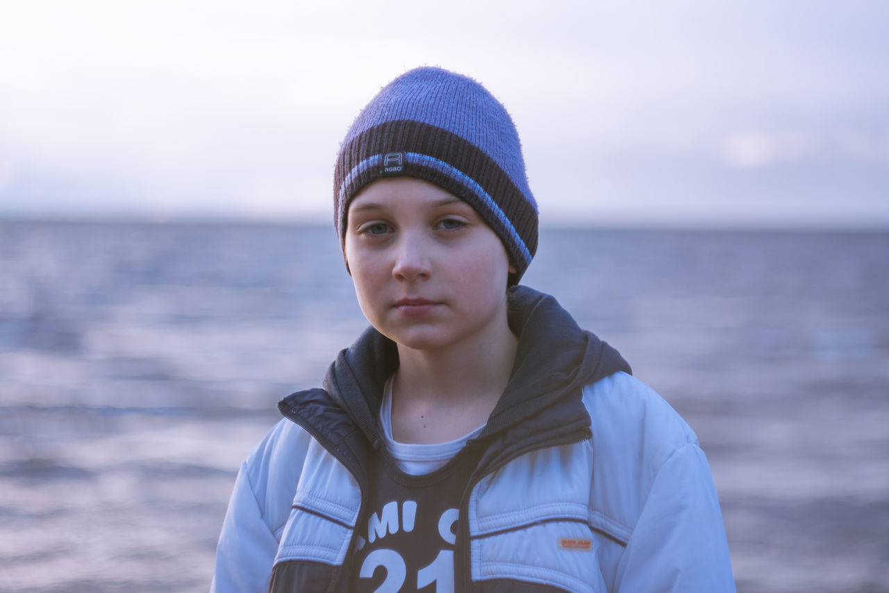 headshot, focus on foreground, sea, front view, leisure activity, water, casual clothing, blue, looking at camera, person, innocence