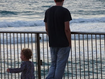 Rear view of men standing by railing against sea