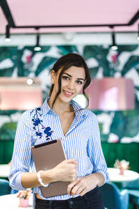 Portrait of smiling businesswoman with digital tablet standing in cafe