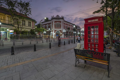 Footpath by street against buildings in city at dusk