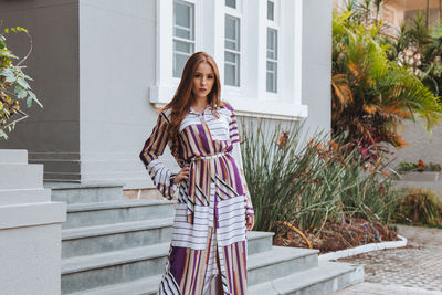 Portrait of young woman standing outside house