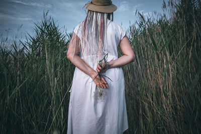 Girl with with unrecognizable face, multicolored braids hold large dandelion