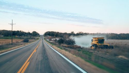 Empty country road by farm against sky