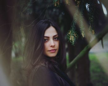 Portrait of beautiful young woman against trees at park