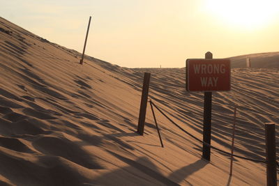 Sign board on sand against sky during sunset