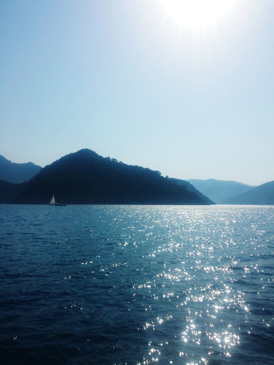 water, mountain, sky, beauty in nature, scenics - nature, tranquil scene, tranquility, sea, sunlight, waterfront, nature, day, clear sky, no people, mountain range, blue, sunny, outdoors, non-urban scene, lens flare, bright