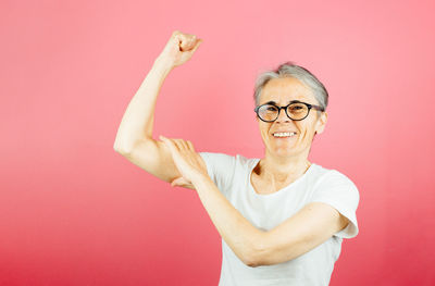 Portrait of young woman with arms raised standing against yellow background