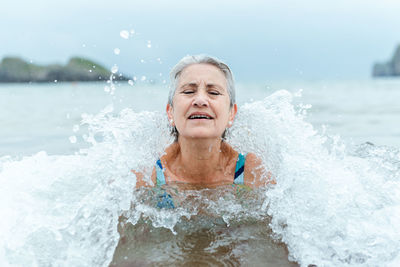 Active senior gray haired female swimming in ocean water while enjoying summertime and practicing healthy lifestyle on seashore