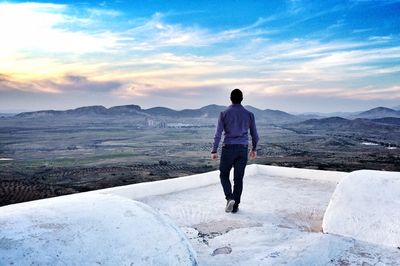 Rear view of man on rooftop against sky during sunset