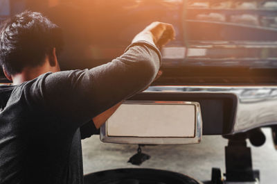 Rear view of man working on car at repair shop