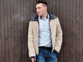 Young man looking away while standing on wooden wall