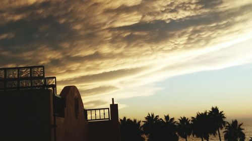 Silhouette palm trees and building against sky at sunset