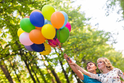 Rear view of woman holding balloons against trees