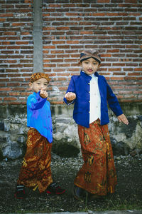 Portrait of cute siblings in traditional clothing against brick wall