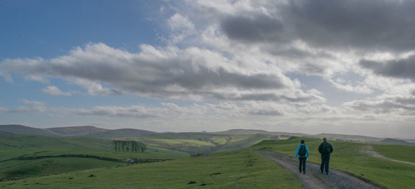 Rear view of friends walking on landscape against cloudy sky