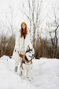 Portrait of young woman standing on snow covered field with dog