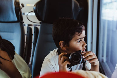 Curious boy with camera looking at window while sitting in train