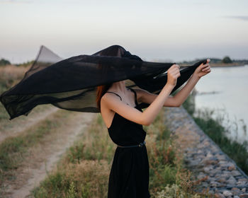 Rear view of woman with umbrella standing against sky