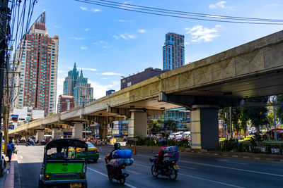 People on city street by modern buildings against sky