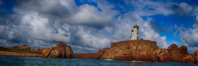 Panoramic shot of rock formations by sea against cloudy sky