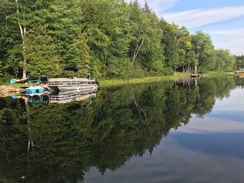 Boats moored on lake by trees against sky