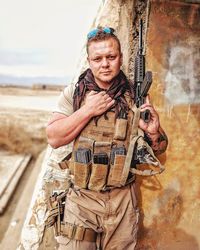 Portrait of male army soldier holding gun against wall