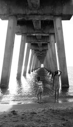 Rear view of sisters standing below pier at beach