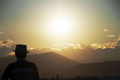 Rear view of silhouette man looking at mountains against sky during sunset