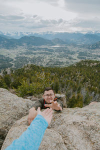 Woman helping a man up from climbing a mountain 