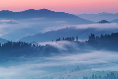 Scenic view of mountains in foggy weather against sky during sunset