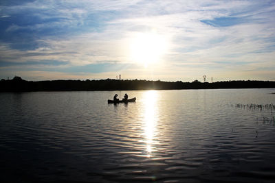 Silhouette people on boat in lake against sky during sunset