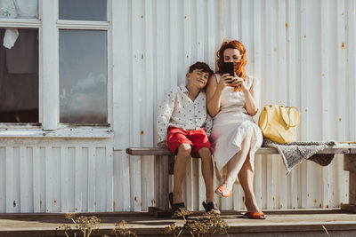 Mother using phone while sitting by son over seat against cabin