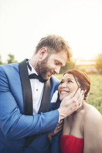 Smiling newlywed couple against sky