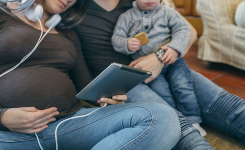 Midsection of parents with son using digital tablet while sitting in living room at home