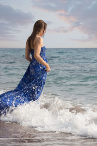 Rear view of young woman standing at beach against sky