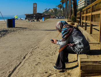 Woman wearing hijab using cell phone at beach