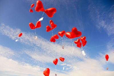 Low angle view of red heart shaped helium balloons flying against sky