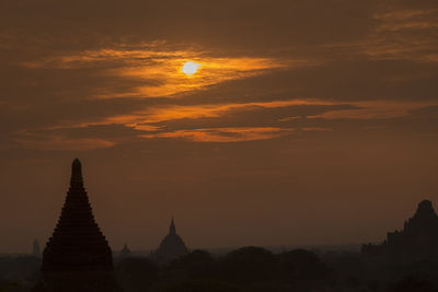 Silhouette stupas against dramatic sky during sunset