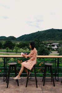 Woman sitting on chair by table against sky