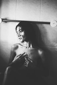 Shirtless woman looking away while sitting in bathroom