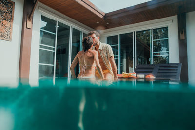 Young woman sitting by swimming pool at window