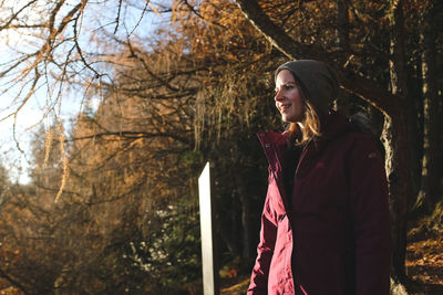 Smiling young woman looking away while standing against trees at forest